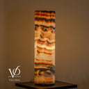 Illuminated Sahara Onyx cylinder table lamp glowing with cream, honey, caramel, and dark brown natural banding
