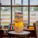 Decorative lamp with multicolored pattern on a wooden table in a room with large windows.