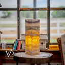 Decorative lamp with multicolored pattern on a round wooden table in a room with large windows.