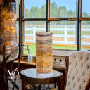 Decorative stone column on a round table with a view of a fenced area outside a large window.