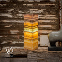 Decorative stone column with multicolored layers on a rustic wooden background, featuring the brand 'Vilona'.