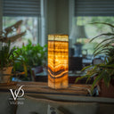 Decorative lamp with a patterned glass shade on a table with plants in a blurred indoor setting, featuring the Vilona brand.