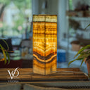 Decorative lamp with layered design on a wooden surface, blurred indoor background