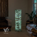Wide room view of an illuminated green Fluorite floor lamp beside a leather sofa, potted plant, and stone table.