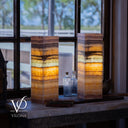 Two layered table lamps on a surface with a blurred window background