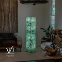 Wide room view of an illuminated Fluorite floor lamp glowing mint green beside a sofa and natural stone furniture.