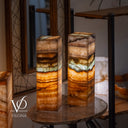 Two onyx column lamps on a round wooden table with a blurred background