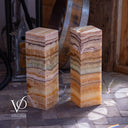 Two onyx columns with layered pattern in a rustic setting, featuring the brand 'Vilona'.