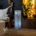 Decorative interior setting with a tall cylindrical light, chair, and decorative elements.