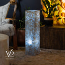 Decorative cylindrical light with a textured surface in a cozy indoor setting, featuring a chair and plants.