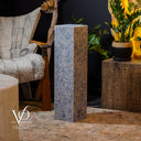 Decorative stone pedestal in a rustic interior setting with furniture and plants.