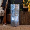 Decorative lamp with a textured surface on a wooden surface, surrounded by plants and furniture.