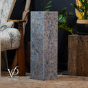 Decorative stone pedestal with a blurred background featuring a chair and plants.
