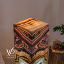 Elevated close-up of the Aqua Onyx lamp’s polished square top and illuminated amber, copper, and cream veining.
