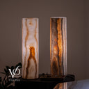 Close front view of a illuminated White Ice onyx lamp pair displayed on a dark pedestal in a warm luxury interior.