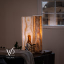 Lifestyle close-up of the glowing White Ice onyx lamp pair styled beside a window and upholstered lounge chair.