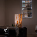 Wide lifestyle view of the White Ice onyx table lamp pair creating warm ambient light beside a window.