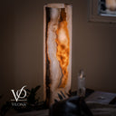 Detailed lifestyle view of the glowing White Ice onyx cylinder lamp styled beside a quartz crystal and leather seating.