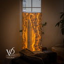Three-quarter view of the illuminated square Golden Cloud onyx tower showing two patterned stone faces beside a window.