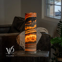 Illuminated Tangerine Onyx table lamp with a broad charcoal band near the rim and glowing honey-colored stone below.