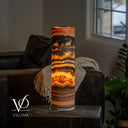 Rear view of an illuminated Tangerine Onyx cylinder lamp with amber and orange bands and a power cord at the base.