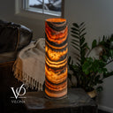 Tangerine Onyx cylinder table lamp glowing on a side table beside a leather sofa, cream throw, and green plants.