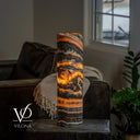 Illuminated Tangerine Onyx cylinder table lamp with amber ribbons winding through charcoal and brown stone.