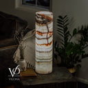 Light Tangerine Onyx table lamp glowing on a dark side table beside a vase, vintage book, leather sofa, and greenery.