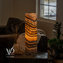 Tangerine Onyx cylinder table lamp glowing amber through angled charcoal bands and fan-shaped crystal formations.