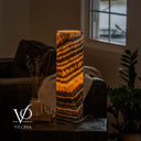Illuminated Tangerine Onyx cylinder lamp with sloping golden bands and a power cord extending to the right.