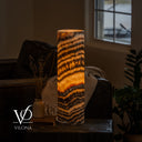 Glowing Tangerine Onyx table lamp with diagonal amber and charcoal bands and a cord visible at the lower left.