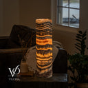 Illuminated Tangerine Onyx cylinder table lamp with rippled charcoal bands above a broad amber-orange ribbon.