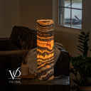 Glowing Tangerine Onyx cylinder lamp with a curved orange formation, golden waves, and diagonal brown layers near the base.