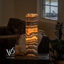Rear view of an illuminated Tangerine Onyx lamp with amber waves, charcoal bands, and a power cord at the base.