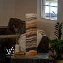 Unlit Tangerine Onyx cylinder lamp with layered ivory and apricot stone above a broad charcoal band and peach crystal base.