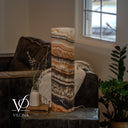 Unlit Tangerine Onyx cylinder lamp with cream and apricot layers, a sweeping charcoal section, and a cord to the right.