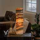 Cord-side view of a glowing Tangerine Onyx lamp with a broad golden center and a white cord crossing the pale base.