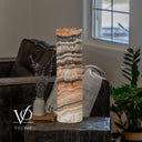 Unlit cord-side view of a Tangerine Onyx cylinder lamp with charcoal, cream, and apricot bands above a white stone base.