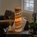 Illuminated Tangerine Onyx cylinder lamp with sloping golden bands, orange seams, and a cord extending to the right.