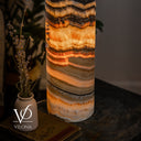 Close-up of the lamp’s lower layers, showing glowing orange ribbons, fine taupe banding, and a creamy white base.