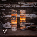 Illuminated Tangerine Onyx cylinder table lamp pair with amber-orange bands, ivory crystals, and charcoal patterns.