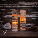 Illuminated cord-side view of two Tangerine Onyx cylinder lamps with glowing amber bands and white cords at both bases.