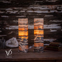 Tangerine Onyx lamp pair illuminated from a third angle, with orange bands and sweeping ivory veins across darker stone.