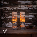 Illuminated Tangerine Onyx table lamp pair styled on a wooden console beside a crystal geode, glass bottles and stacked books.