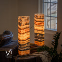 Illuminated Tangerine Onyx lamp pair with curling dark markings near the front lamp’s rim and broad golden crystal bands.
