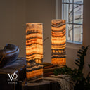 Illuminated Tangerine Onyx lamp pair focused on the rear lamp, with sweeping amber bands and charcoal marbling.