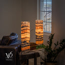 Tangerine Onyx lamp pair glowing beside a leather sofa, styled with books, a cream throw and greenery near a window.