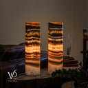 Illuminated Tangerine Onyx lamp pair from another angle, with dark upper layers, glowing amber centers and narrow orange ribbons below.