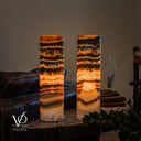 Illuminated Tangerine Onyx lamp pair with charcoal bands and a large rounded amber crystal formation on the right lamp.
