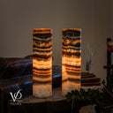 Illuminated Tangerine Onyx lamp pair with curved golden banding on the right lamp and the left lamp’s cord visible at its base.